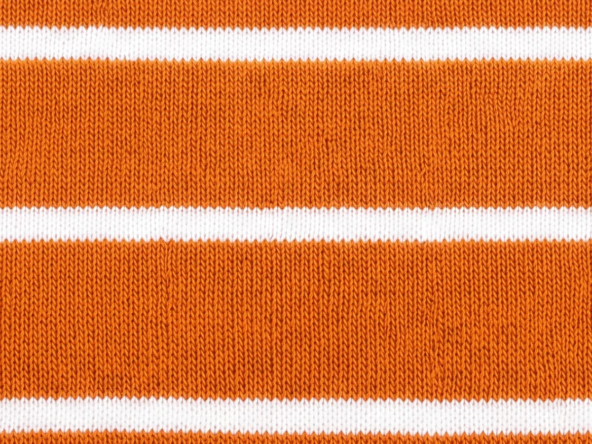 Close view of an orange interlock knit with white stripes across it