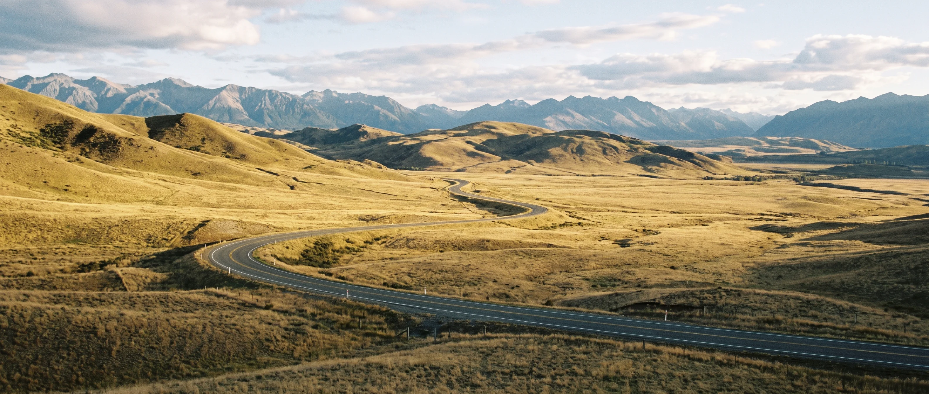 Long empty road curving away through dry rolling hills at the end of the day