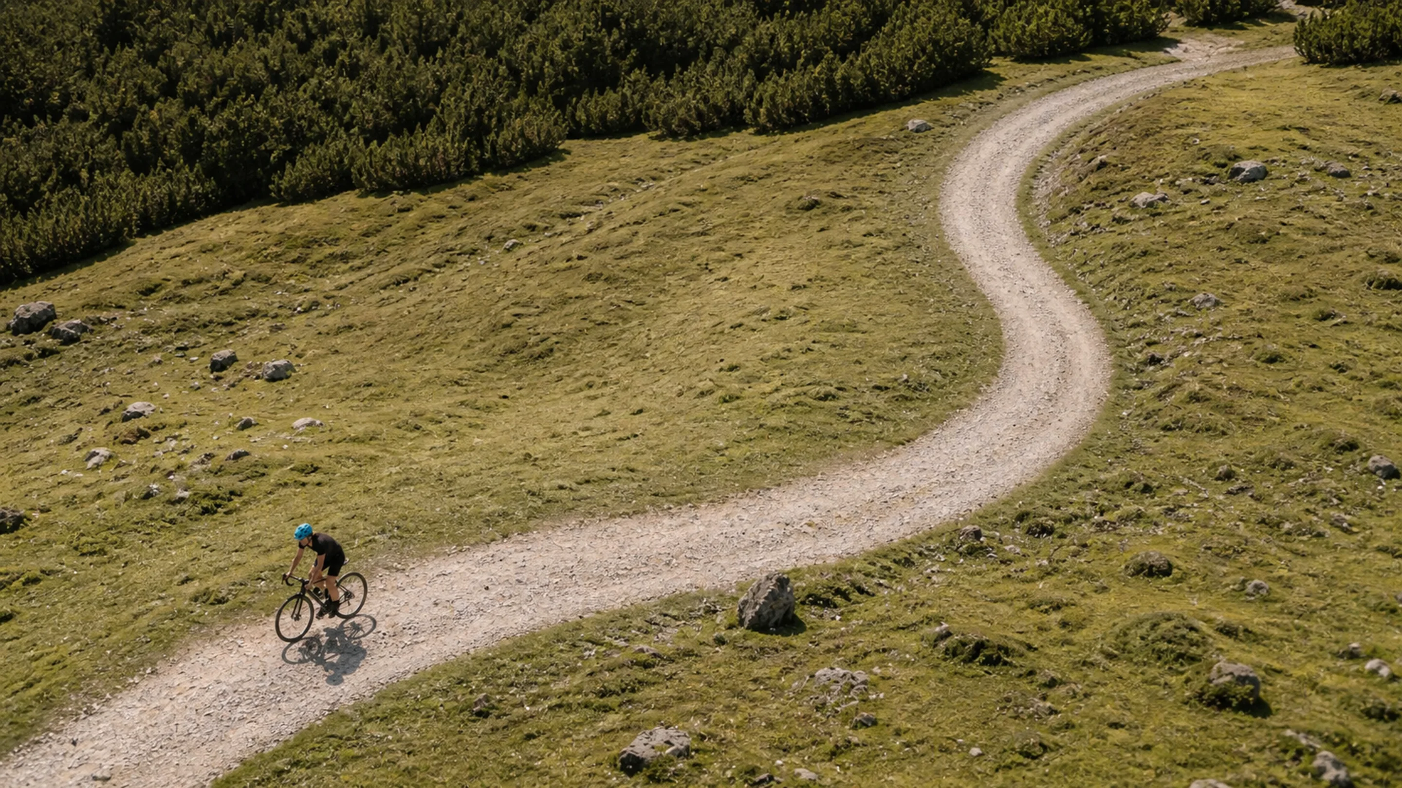 Cyclist riding a winding gravel path through open hill country, seen from above