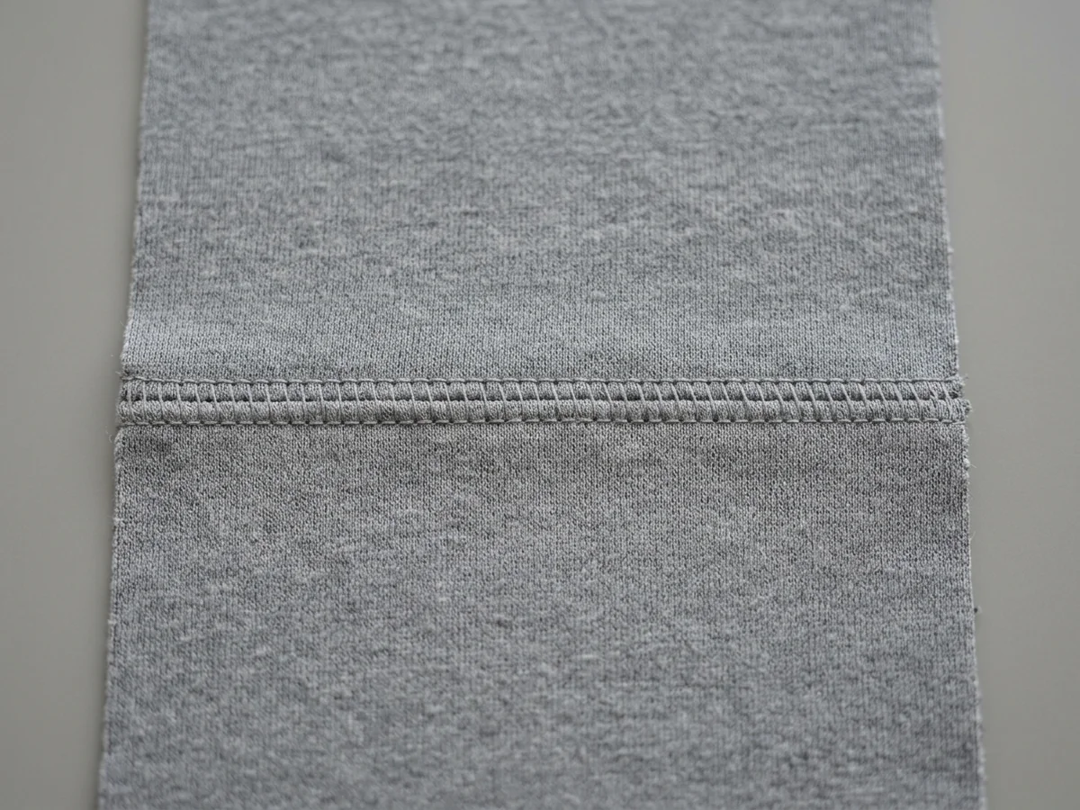 Macro of a flat seam on the same grey performance knit, two panels joined by an even row of coverstitching sitting almost level with the cloth