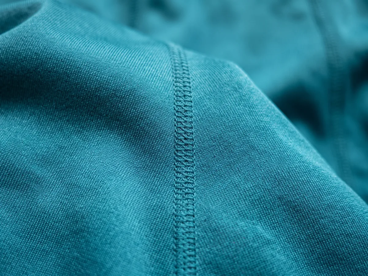 Close-up of a teal synthetic performance fabric, its surface gathered into folds and catching the light unevenly