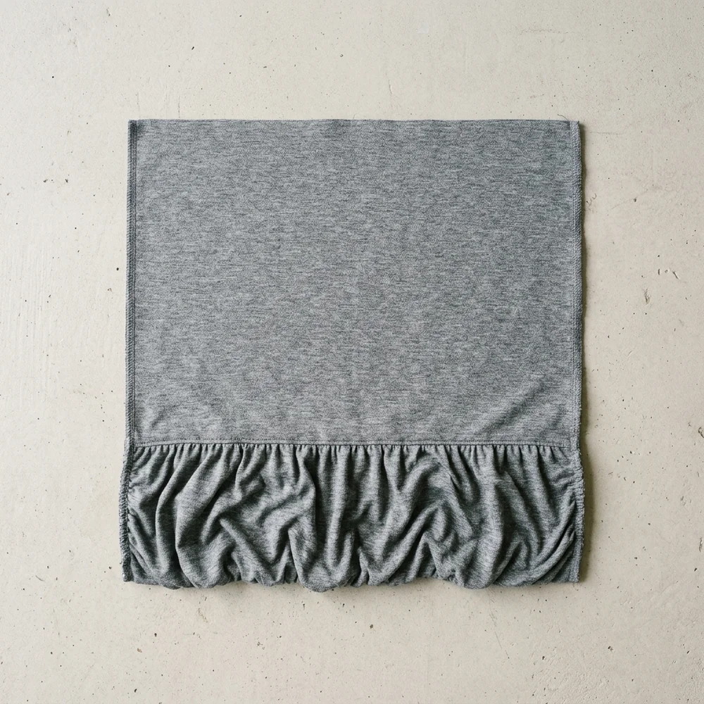 A flat grey knit panel seen from above with a broad band of gathered fullness worked in low across the bottom edge